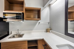 Una cocina con microondas integrado, pileta de acero inoxidable, armarios de madera y encimera con motas blancas.
