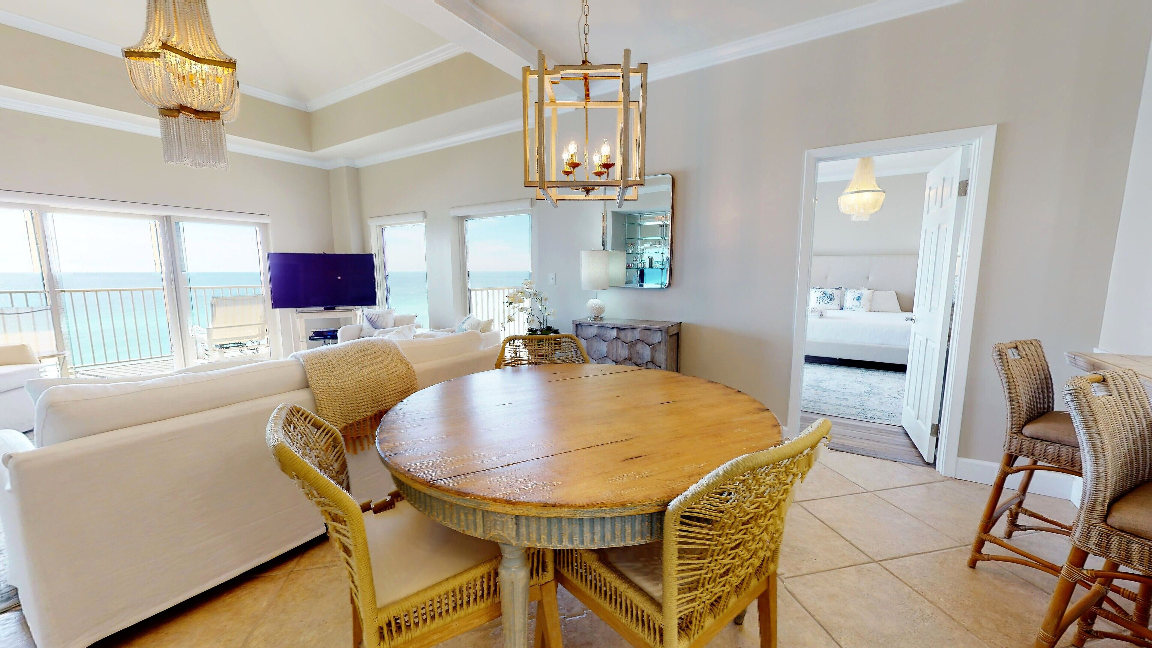 A spacious living area with a round wooden dining table, wicker chairs, a white sofa, and a television.