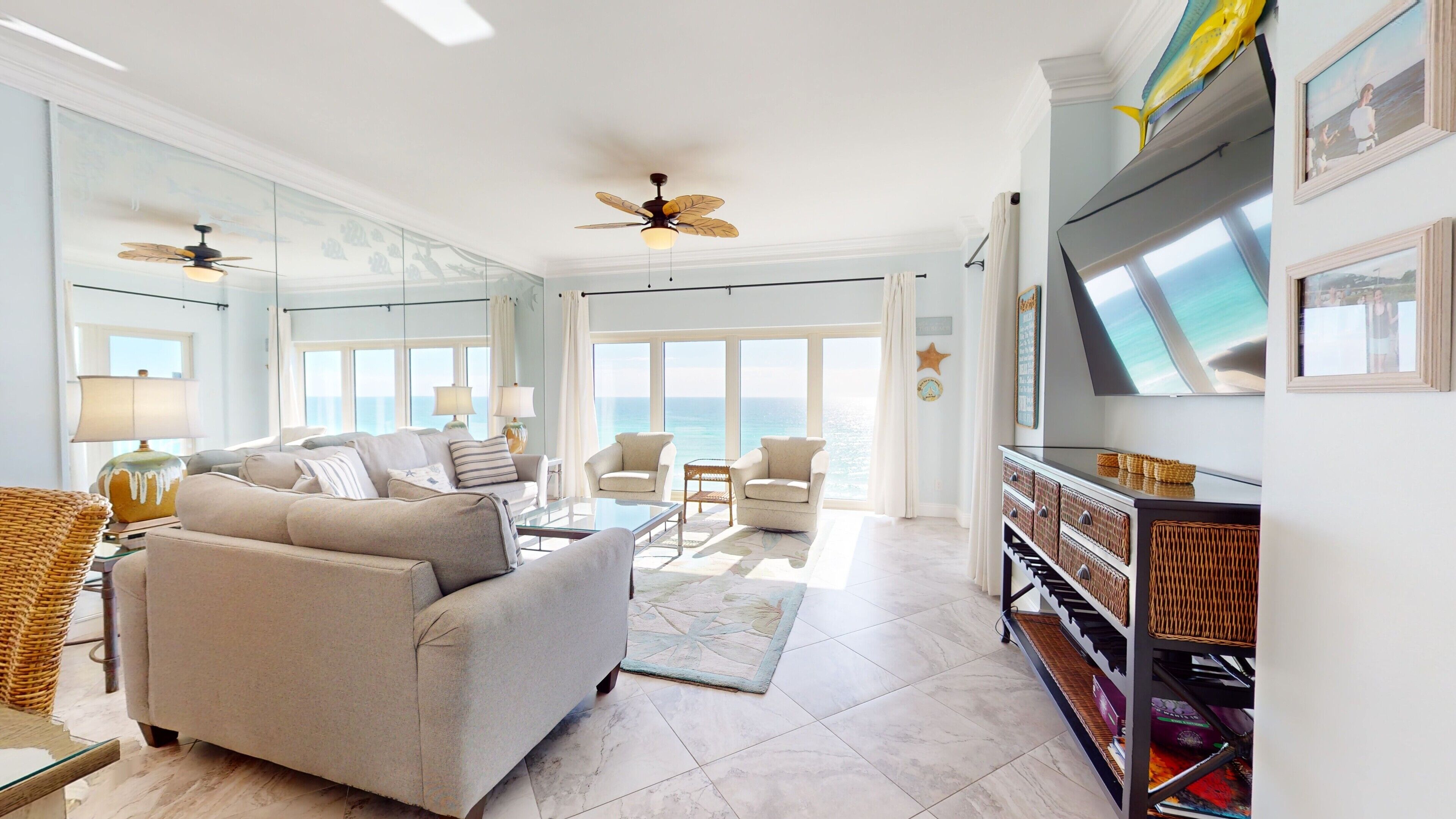 A spacious living room with a large TV, comfortable seating, and a view of the ocean.
