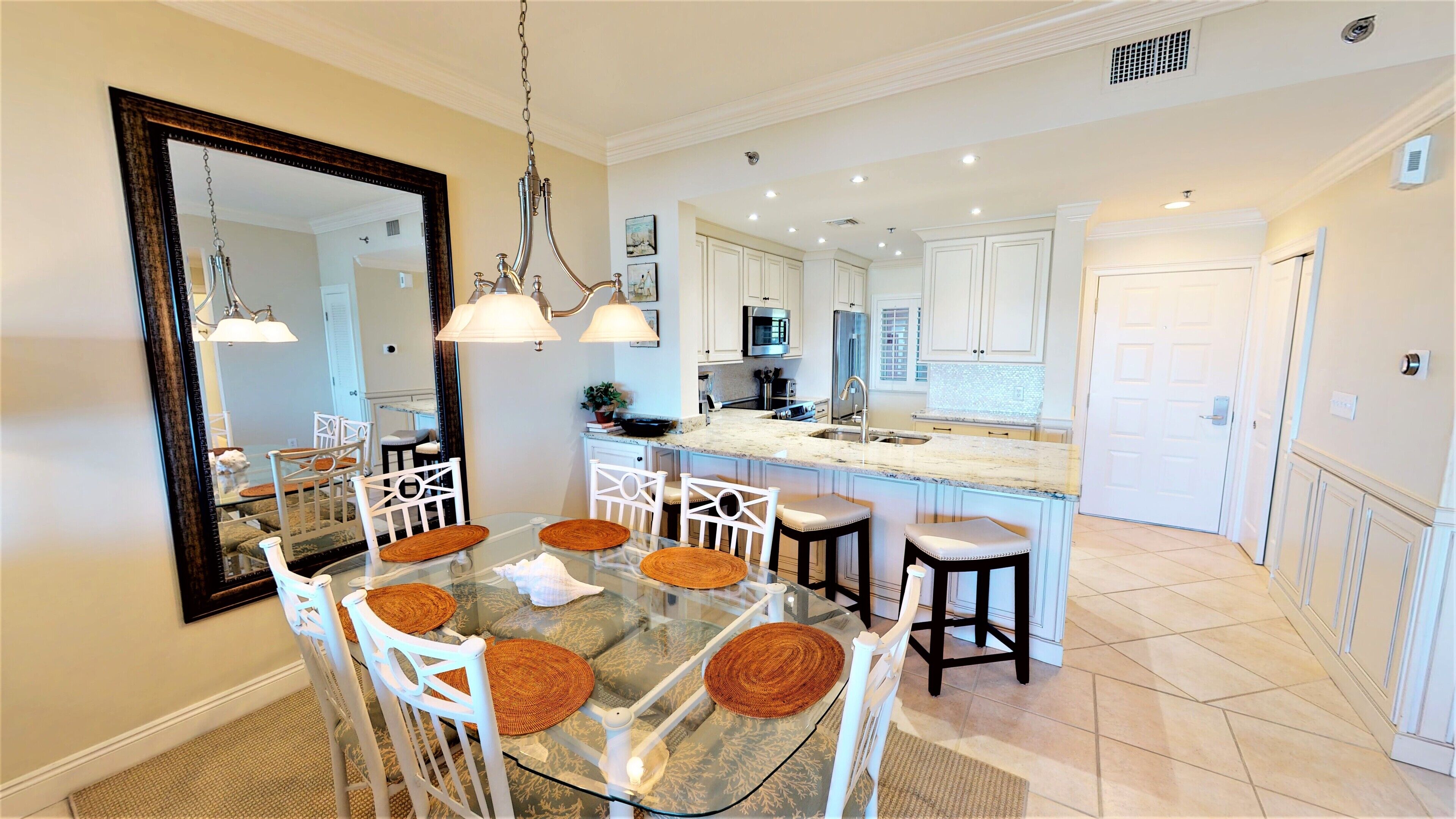 A modern kitchen with white cabinets, a large island, and a dining area with a glass table and white chairs.