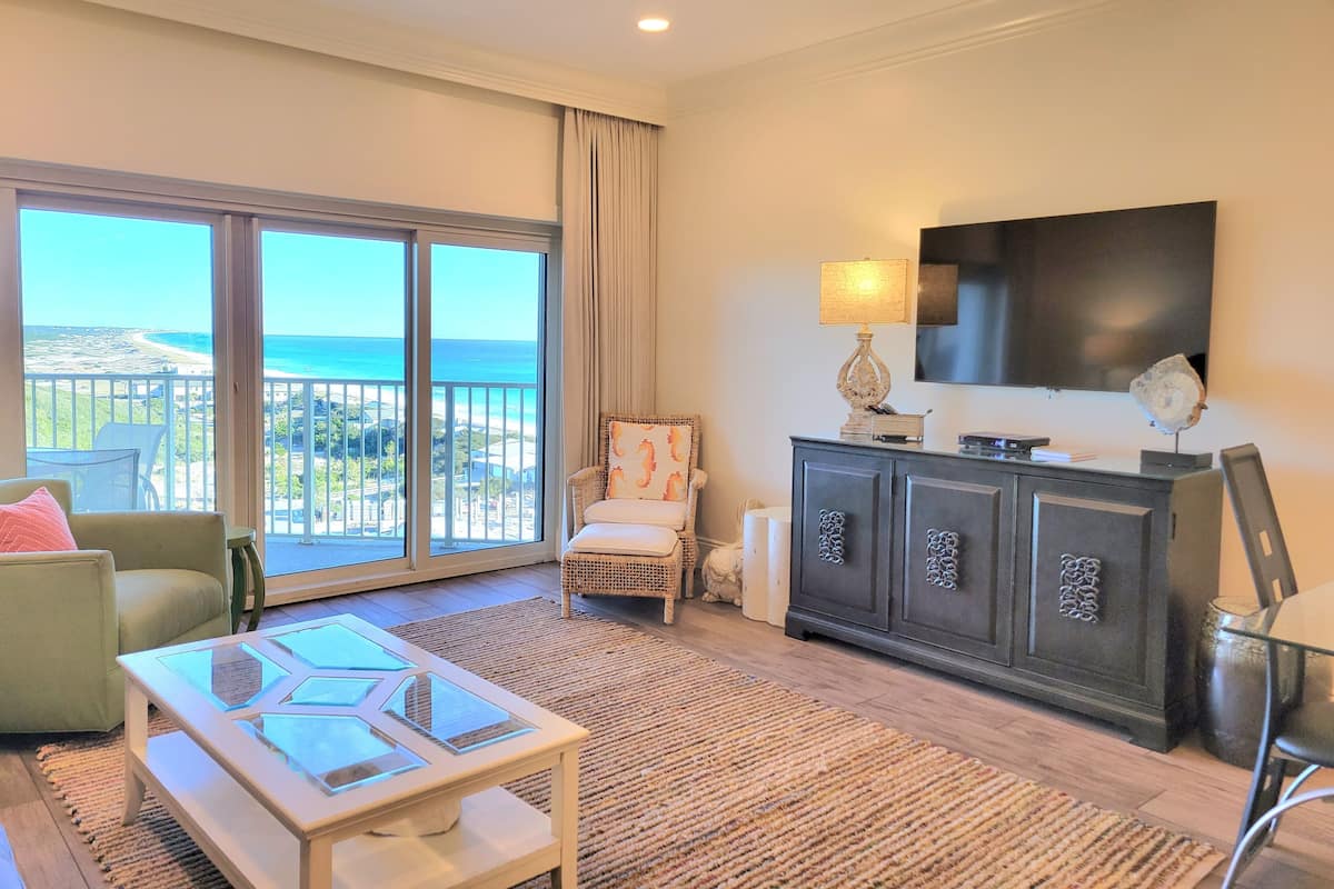 A spacious living room with a large balcony, a flat-screen TV, and a modern fireplace.