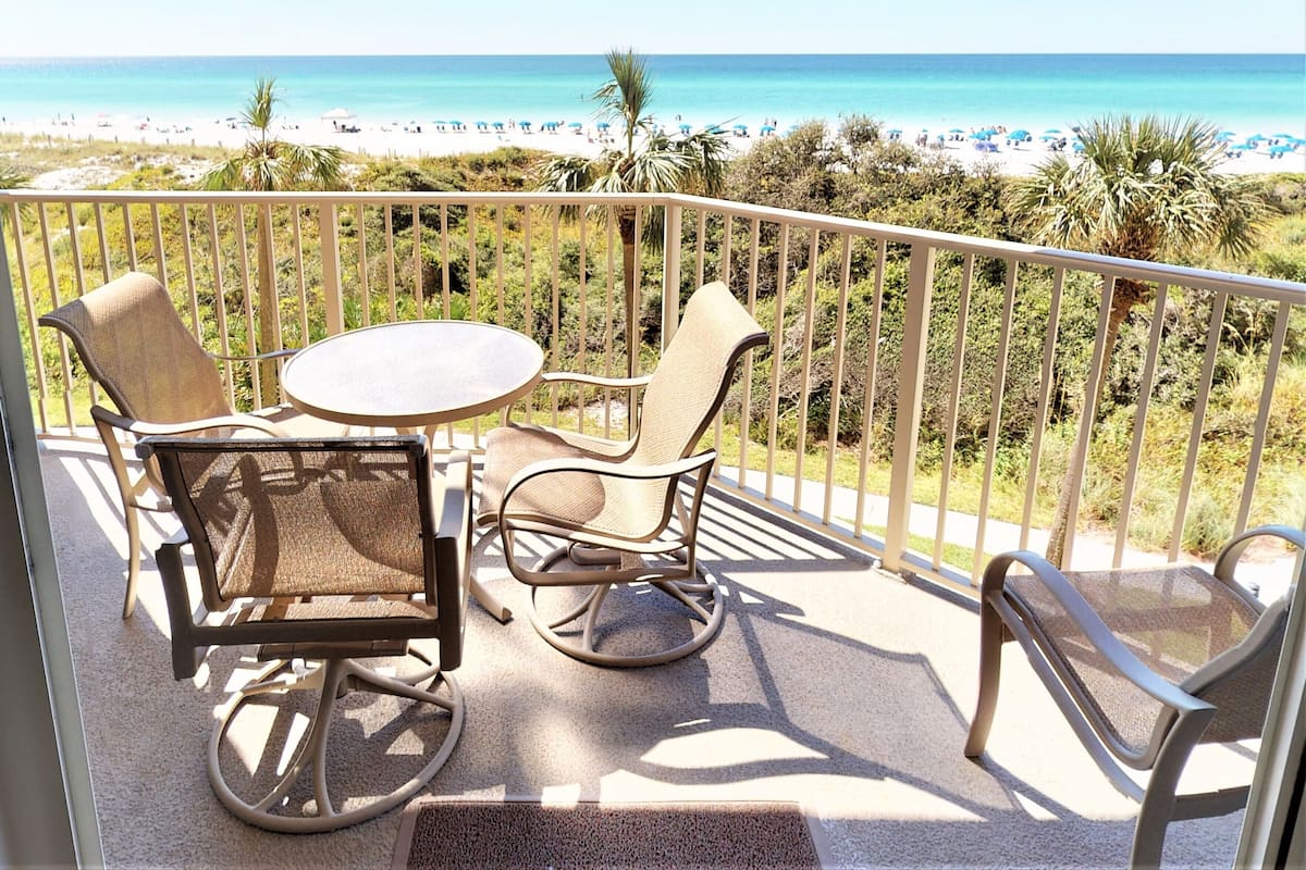 A balcony with a table and chairs overlooking a beach.