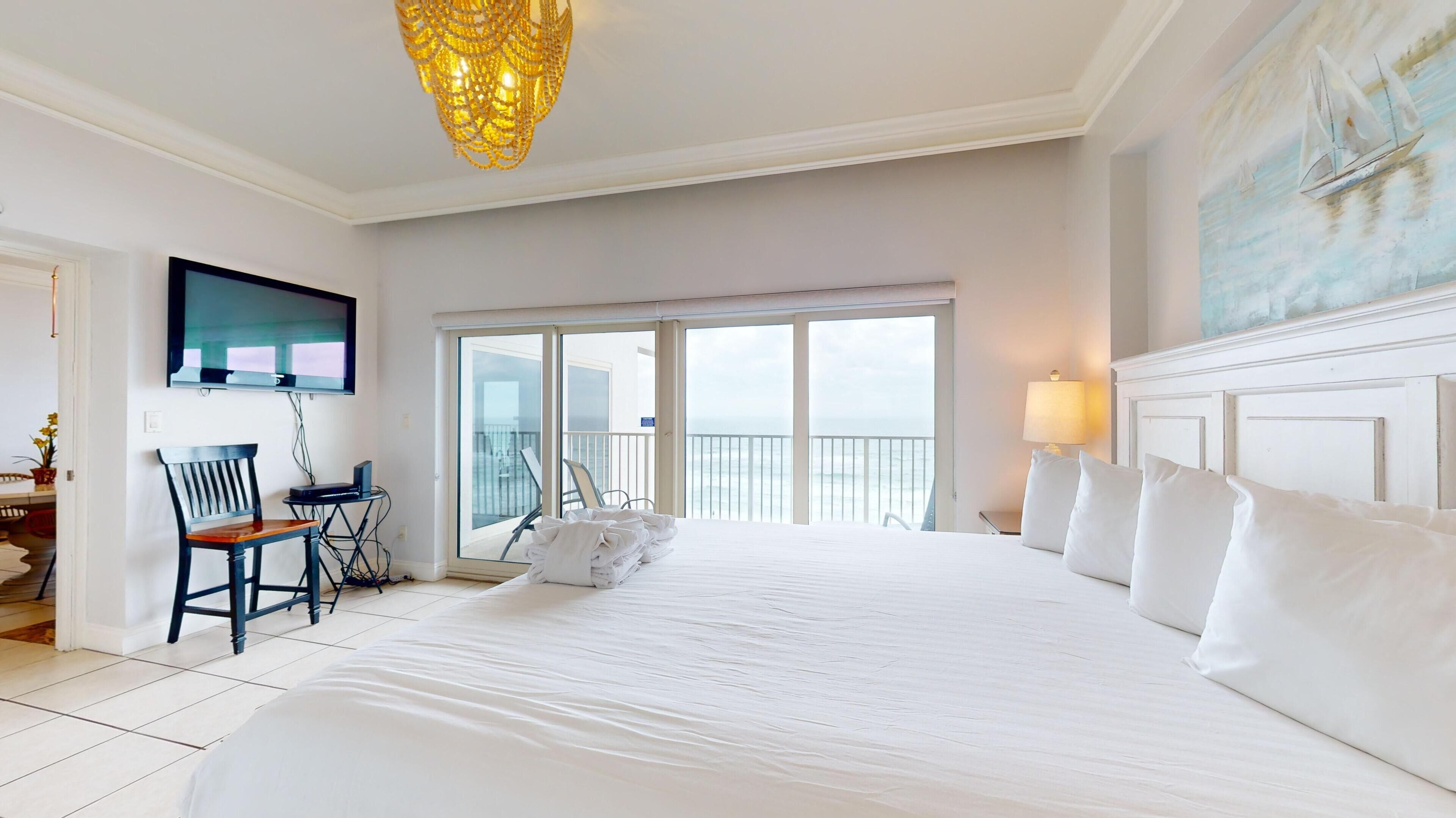 Ein Hotelzimmer mit einem großen Bett, einem Schreibtisch mit Stuhl, einem Fernseher und einem Balkon mit Aussicht.