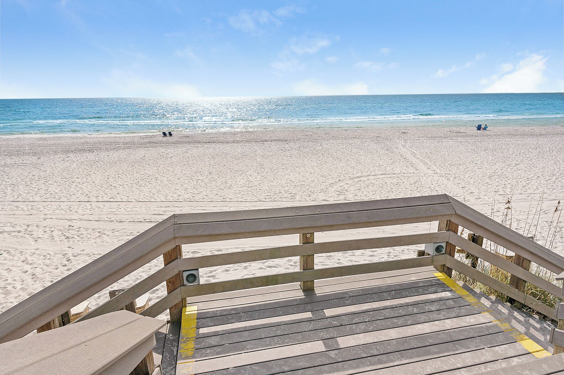 A wooden boardwalk leading to a sandy beach with a clear view of the ocean.