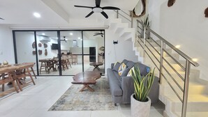 Ein modernes Wohnzimmer mit grauem Sofa, Esstisch aus Holz und einer Treppe mit Metallgeländern.