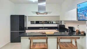 Eine moderne Küche mit einem schwarzen Kühlschrank, einer Edelstahl-Dunstabzugshaube, einer schwarzen Arbeitsplatte und zwei Holzhocker.