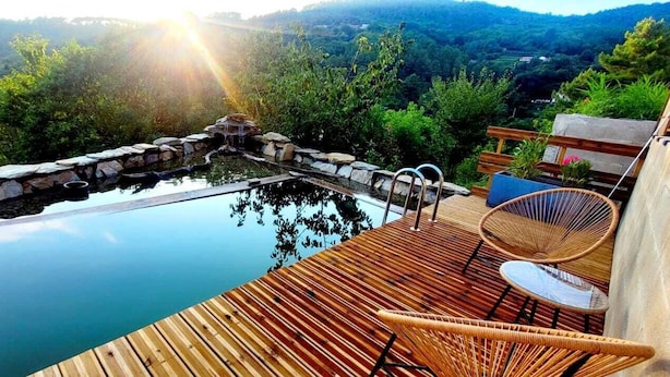 A wooden deck with a pool, wicker chairs, and a stone waterfall feature. - Mas de 130m2 en Plein Cœur des Cévennes sur 12 Hectares (Lamelouze)