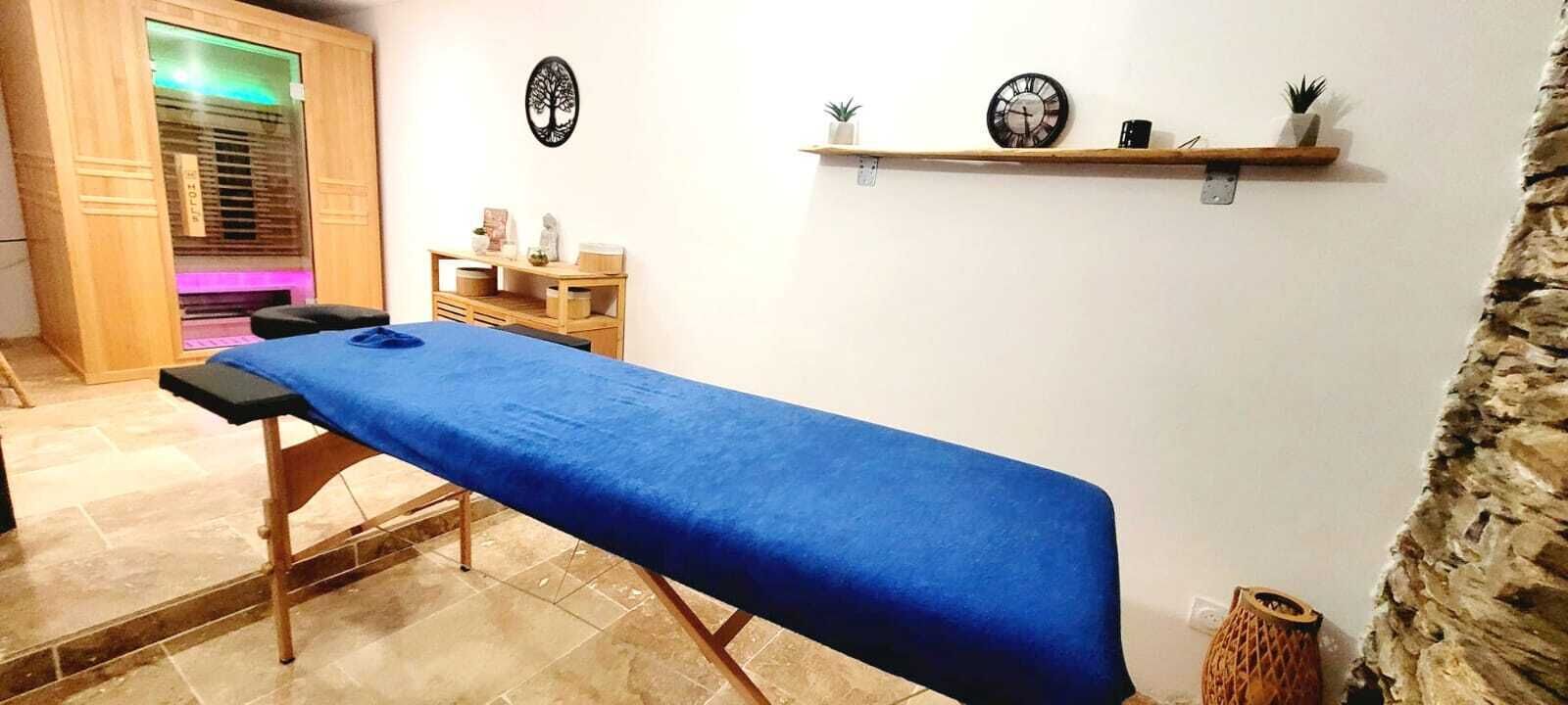 Une pièce comprenant une table de massage, des meubles en bois, une étagère avec des objets décoratifs et un mur en pierre.