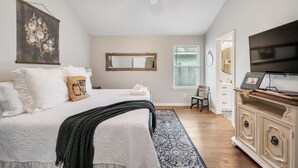 Un dormitorio con cama, ventilador de techo, espejo grande, televisor y cómoda.