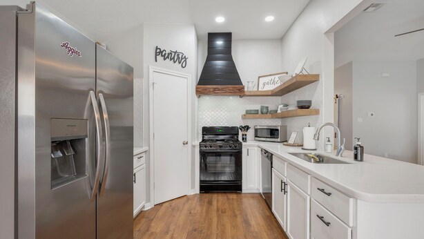 Una cocina moderna con refrigerador de acero inoxidable, extractor de aire negro, microondas y muebles de cocina blancos.