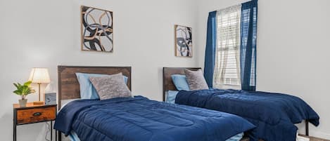 A bedroom with two beds, a nightstand with a lamp, and artwork on the walls.