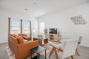 Un salon moderne comprenant un canapé, un fauteuil, une table basse, un téléviseur et des œuvres d’art décoratives au mur.