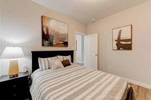 A bedroom with a bed, a nightstand with a lamp, and two wall-mounted paintings.