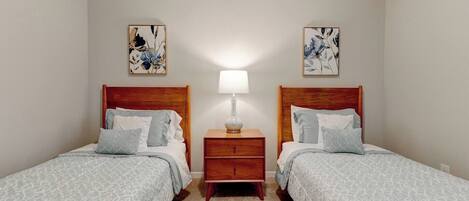 Una habitación con dos camas individuales, una mesita de noche con lámpara y dos cuadros colgados en la pared.