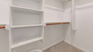 A corner closet with white walls, a wooden rod, and three shelves.