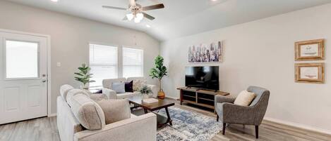 A living room with a sofa, armchair, coffee table, TV, and artwork on the wall.