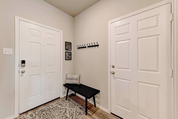 A hallway with two white doors, a bench, a rug, and a coat rack with coats. - Spacious Home in South Temple with 5 Beds (Temple)