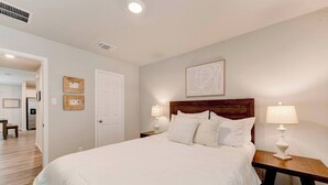 A bedroom with a large bed, two bedside tables with lamps, a wooden headboard, a white door, and a framed artwork on the wall. - Spacious Home in South Temple with 5 Beds (Temple)