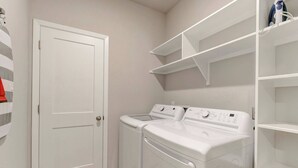 A laundry room with a white door, two stacked washing machines, and white shelving units. - Spacious Haven for Workers in South Temple (Temple)