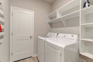 A laundry room with a white door, two stacked washing machines, and white shelving units. - Spacious Haven for Workers in South Temple (Temple)