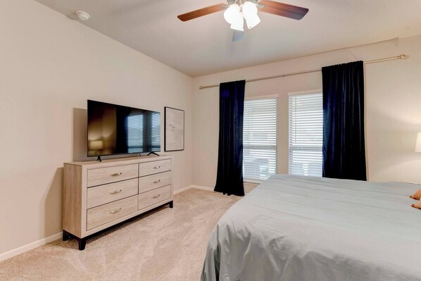 A bedroom with a bed, a dresser, a television, and a ceiling fan.