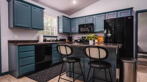 Cuina moderna amb armaris verds mares, un refrigerador negre i dos tamborets.