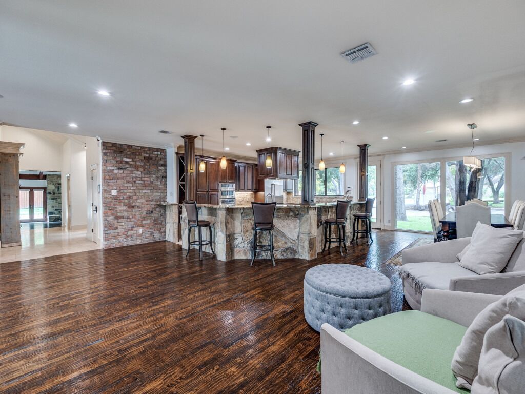 A spacious living area with a kitchen island, dark wooden flooring, and a large window providing natural light.