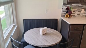 Un comedor con una mesa redonda, cuatro sillas, un adorno de pared y una zona de cocina con armarios y encimera.