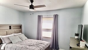 A bedroom with a bed, a ceiling fan, a window with curtains, a dresser, and a TV on a stand. - Cozy 2-bedroom condo in pleasant Elm Grove with AC, WiFi (Elm Grove)