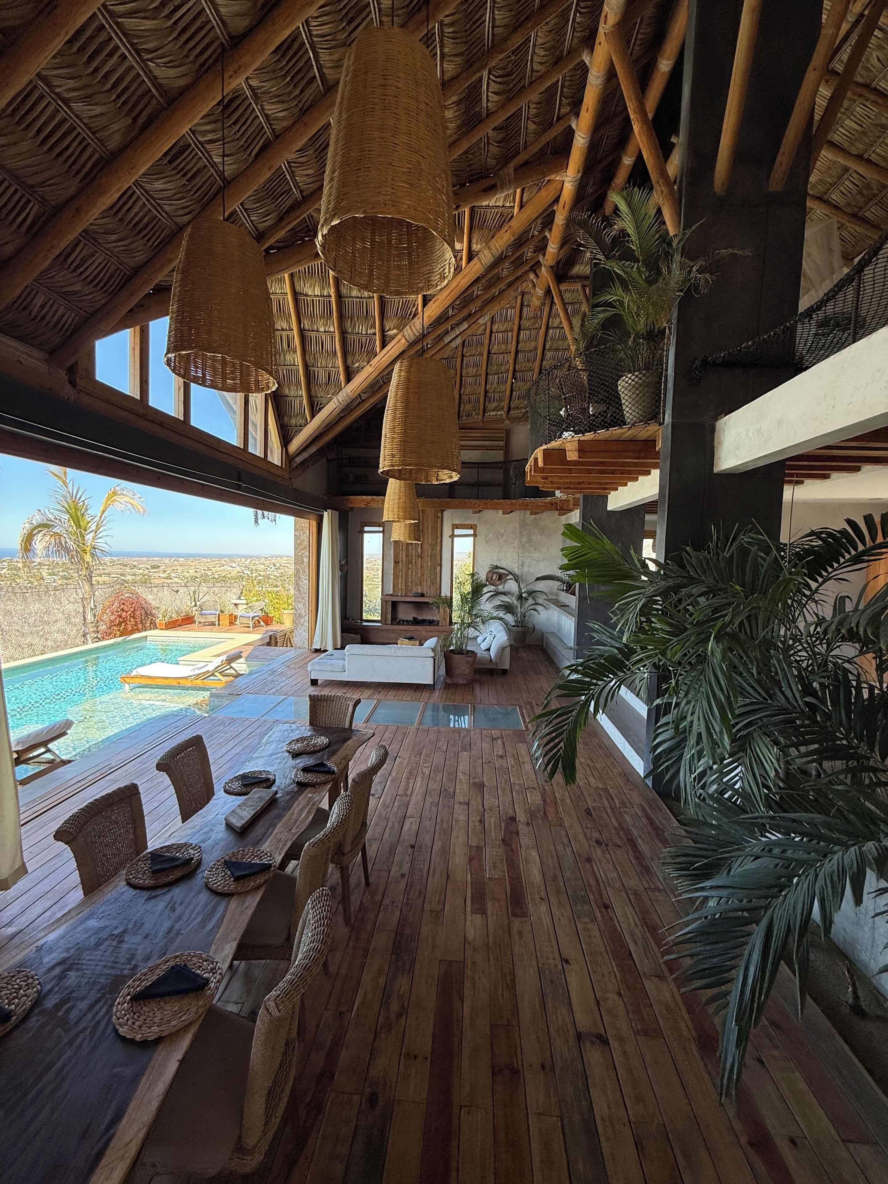 Une terrasse en bois avec une piscine, des meubles en osier et une vue sur l’océan.