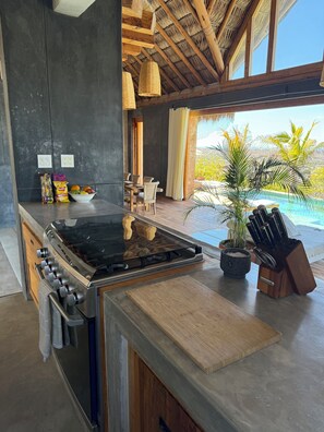 A modern kitchen with a large stove, a dining area with chairs, and a view of a pool. - Las Nubes en Todos Santos  adults only (Todos Santos)