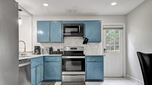 A kitchen with blue cabinets, a microwave, an oven, a coffee maker, and a window. - Charming 3-bedroom bungalow with WiFi in Bham, 12 mins from UAB. (Birmingham)