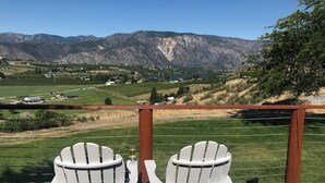 Two white Adirondack chairs facing a scenic view of mountains and a green landscape.