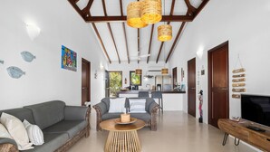 A modern living room with a grey sofa, wicker chairs, a round wooden coffee table, and a TV on a wooden stand. - Villa with 2 bedrooms, big porch and amazing ocean view
 (Kralendijk)