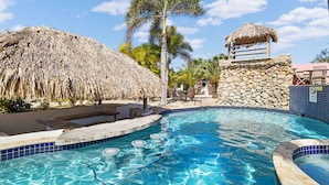 A swimming pool with clear blue water, a thatched-roof structure, and a stone wall. - Villa with 2 bedrooms, big porch and amazing ocean view
 (Kralendijk)