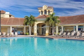 A pool area with lounge chairs and a building with a tiled roof.