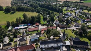An aerial view of a small town with a mix of residential and commercial buildings, surrounded by green fields and forests. - Ferienwohnung Plohn_immo-franzi (Lengenfeld)