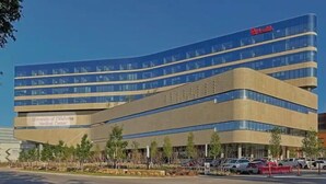 A modern building with a curved facade, a prominent sign for the University of Oklahoma Medical Center, and a parking lot with several cars.