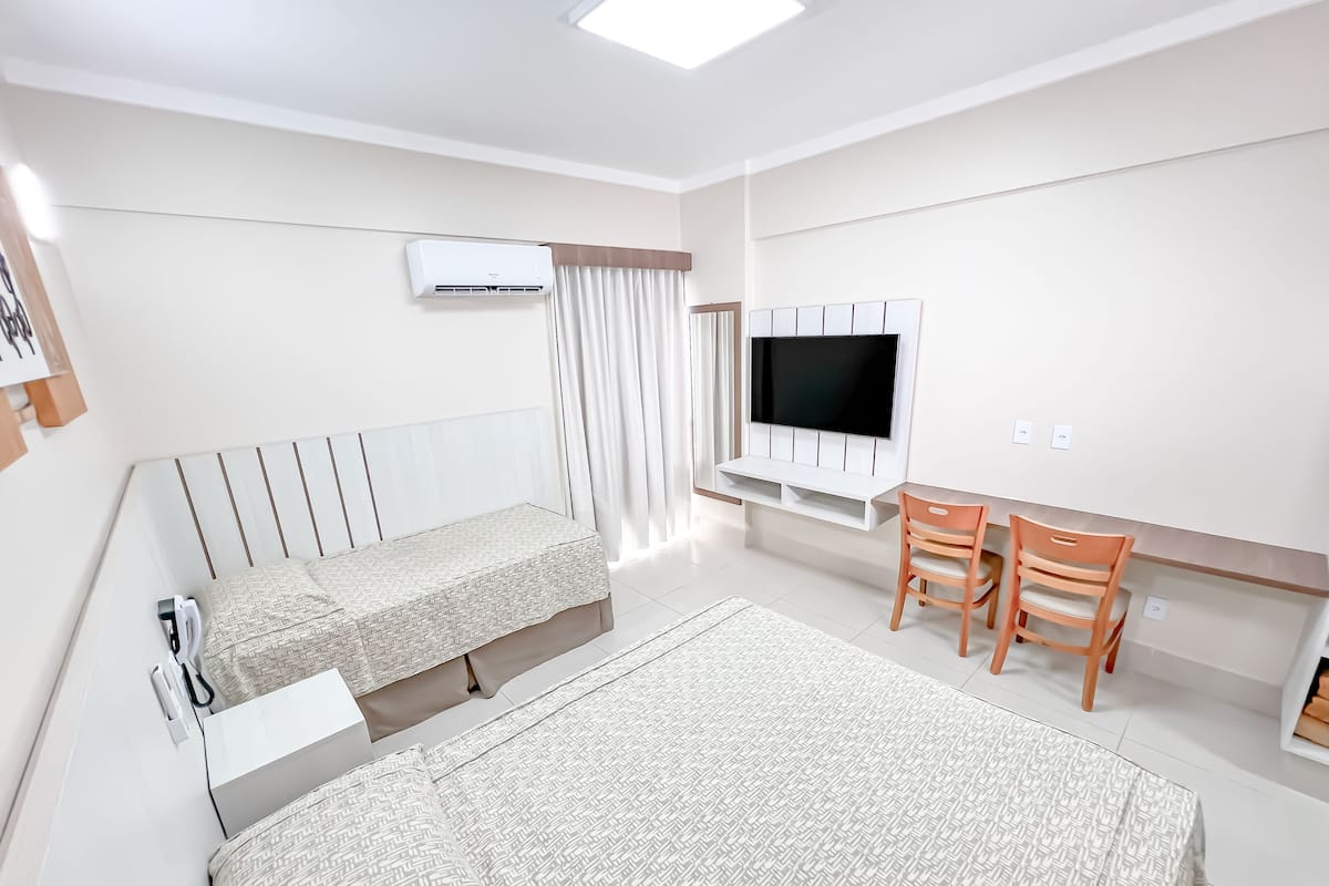 Ein modernes Hotelzimmer mit einem großen Bett, einem Schreibtisch mit zwei Stühlen, einem Flachbildfernseher und einem Fenster mit Vorhängen.