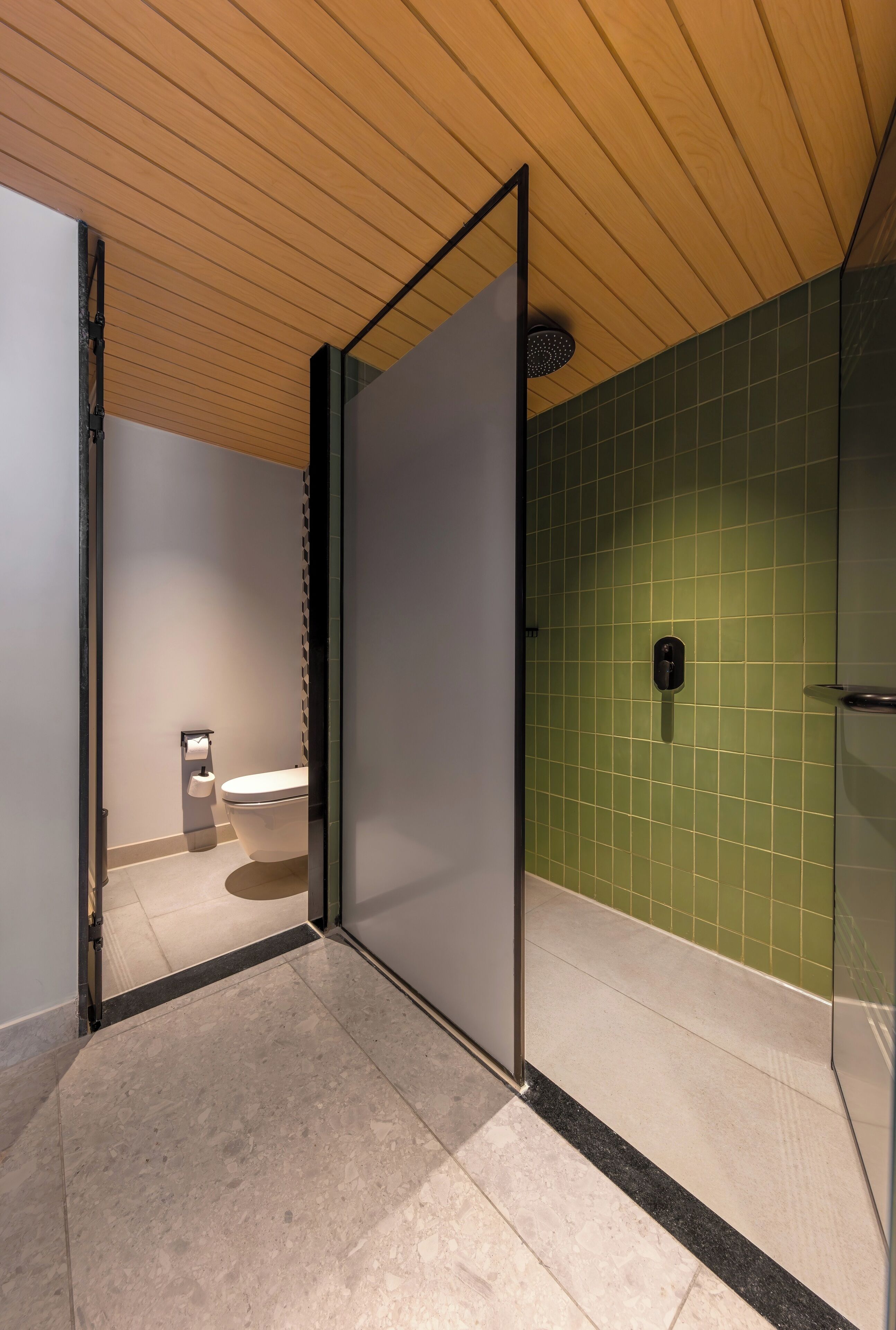 A modern bathroom with a toilet, a shower, and a green tiled wall.