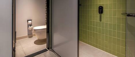 A modern bathroom with a toilet, a shower, and a green tiled wall.