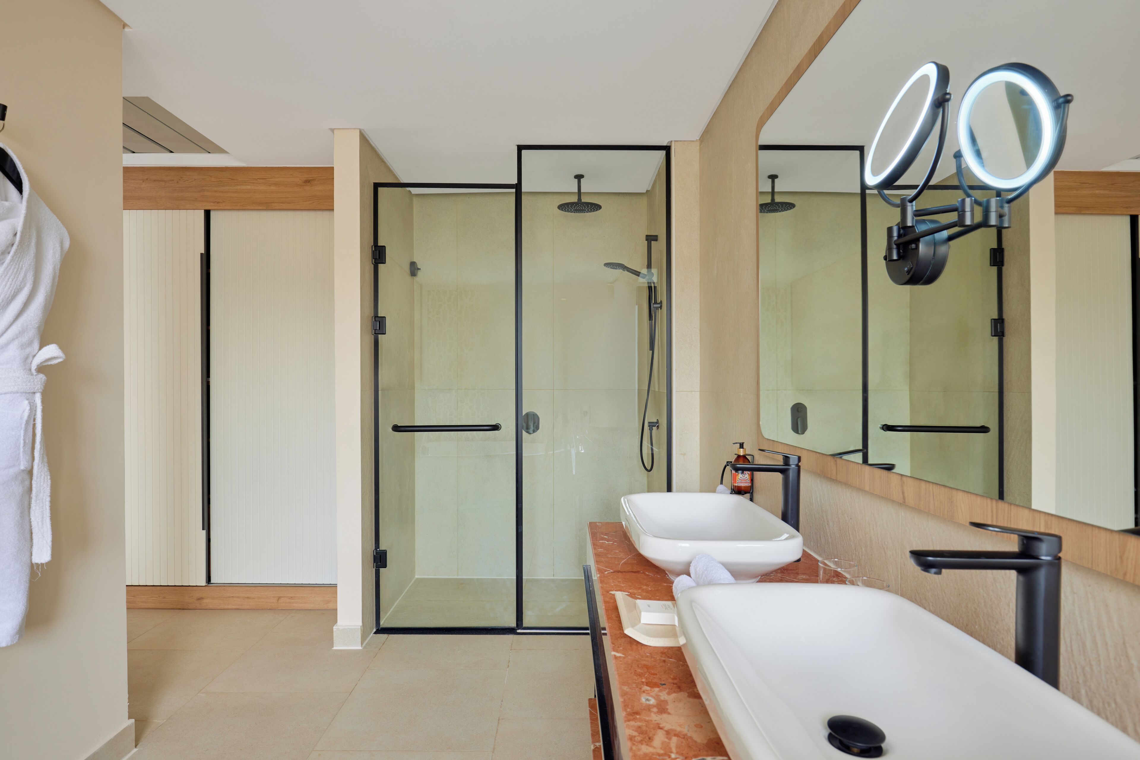 A modern bathroom with a glass shower enclosure, a vanity with a large mirror, and a robe hanging on a hook.