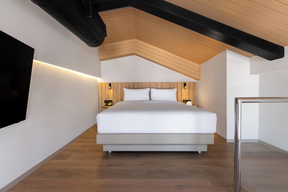 A modern bedroom with a large bed, wooden ceiling beams, and bedside lamps.