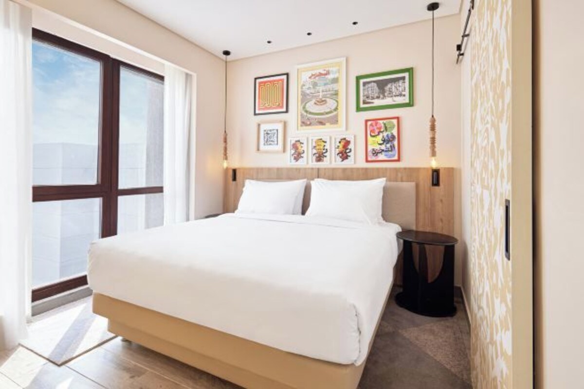 Una camera d'albergo moderna con un letto grande, una testiera in legno e una grande finestra.
