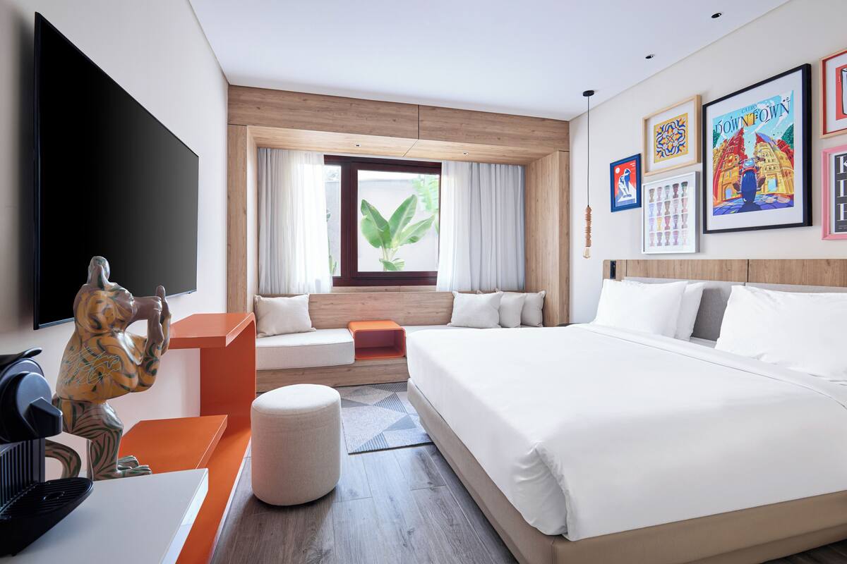 A hotel room with a large bed, a seating area with a view of the outdoors, a flat-screen TV, and artwork on the walls.