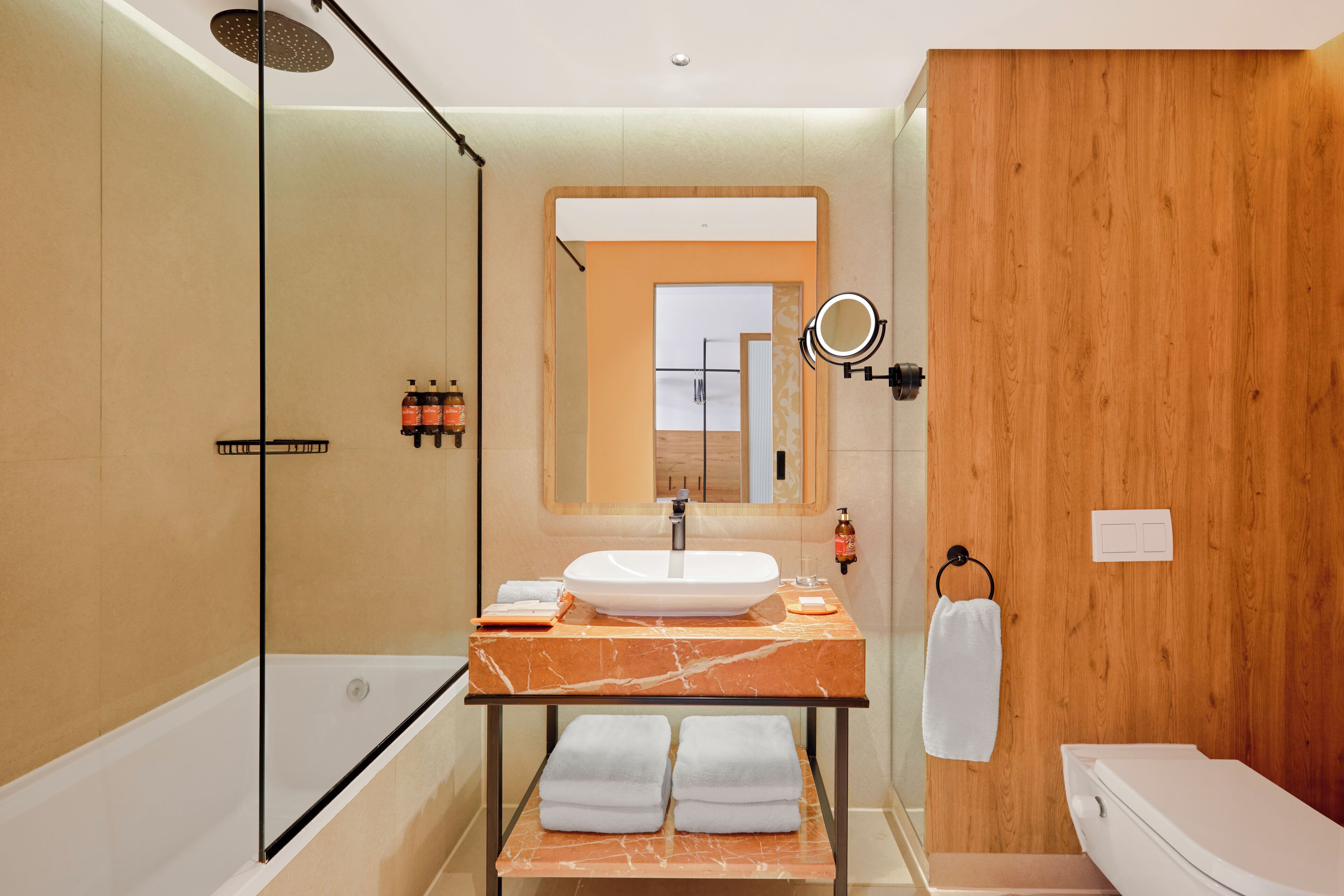 Un baño moderno con ducha de vidrio, lavamanos de mármol y una pared de acento de madera.