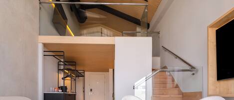 Un interior moderno con una escalera estilo loft, una zona de comedor con dos sillas, un sofá y una pequeña mesa redonda.