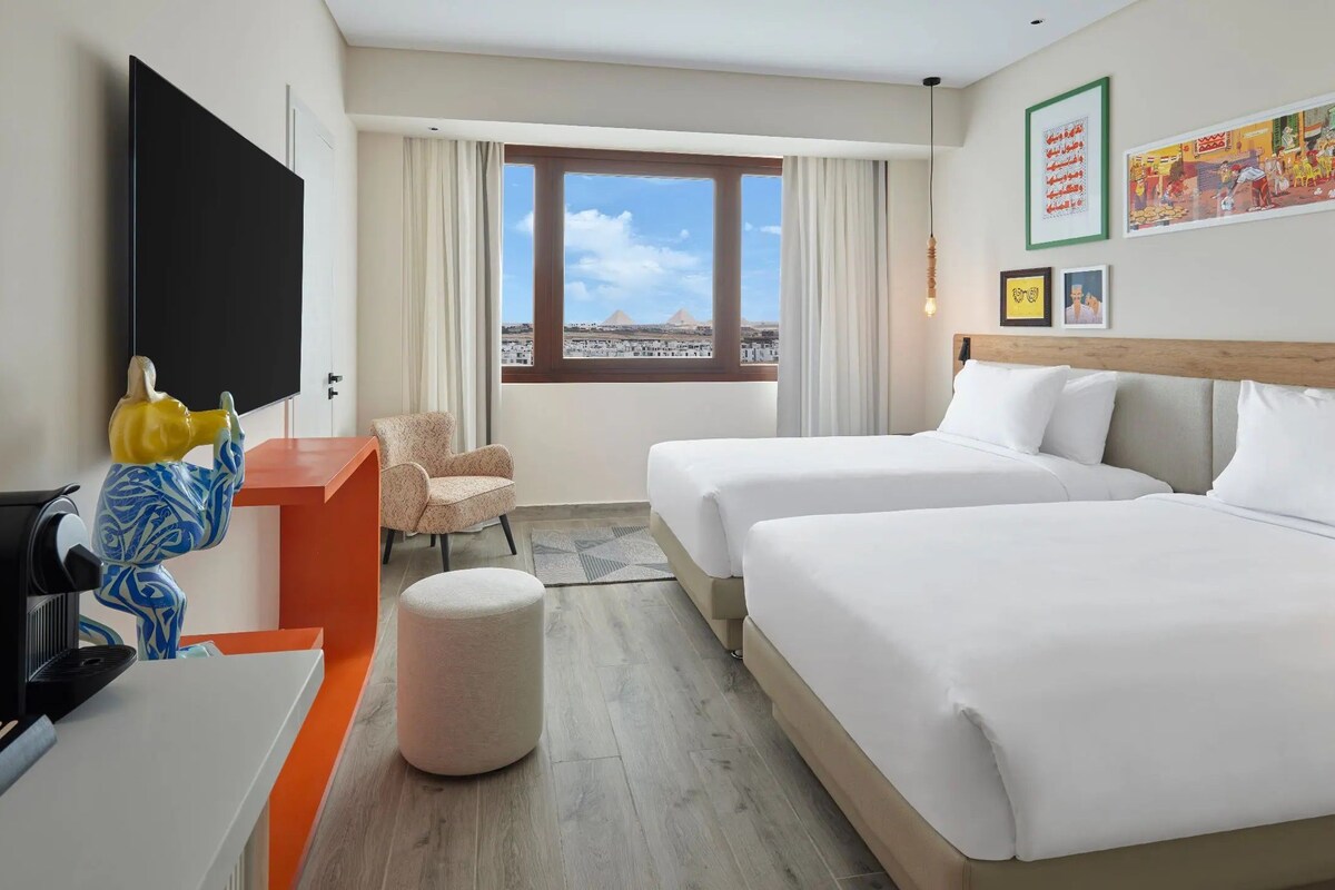 A hotel room with two beds, a TV, a coffee machine, and a window with a city view.