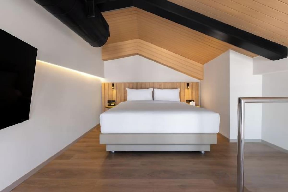 A bedroom with a large bed, wooden ceiling beams, and wall-mounted lighting.