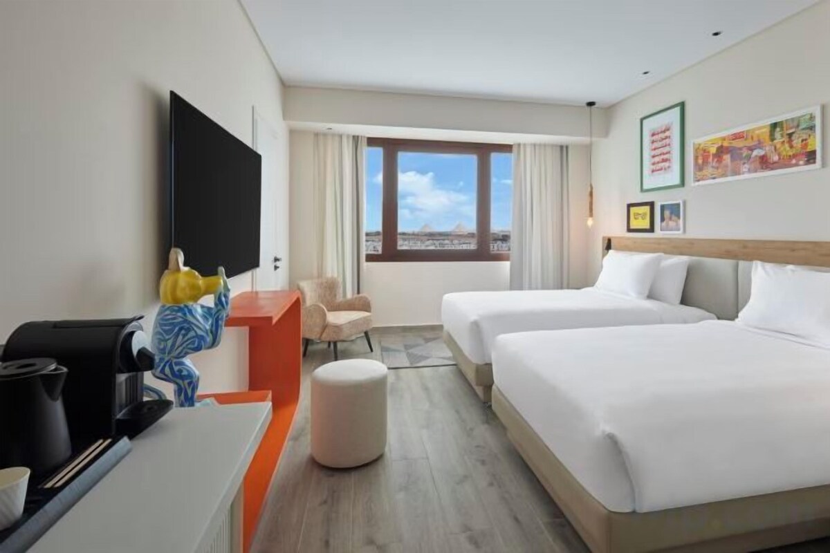 A hotel room with two beds, a desk, a chair, a television, and a window with a view.